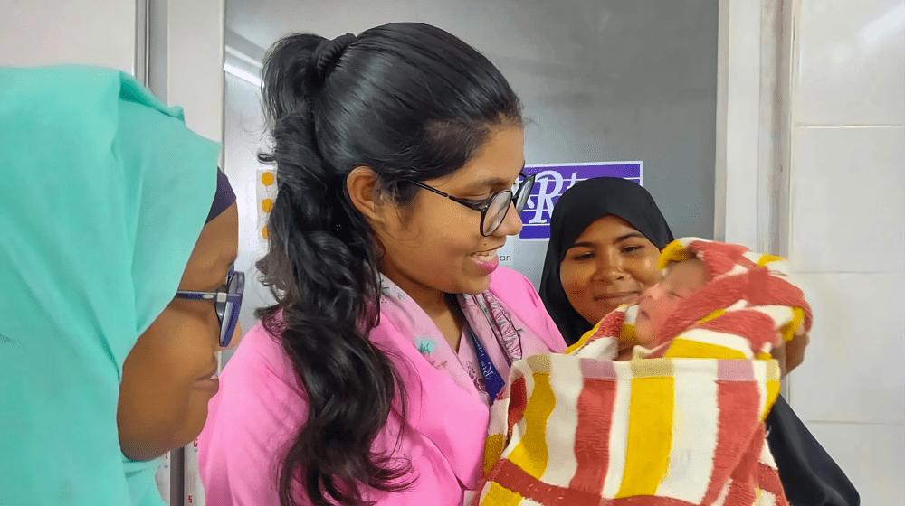 From left to right: Midwife Tamanna Jahan, Midwife Arafin Mim, and the baby’s mother gaze at a newborn they helped safely deliver